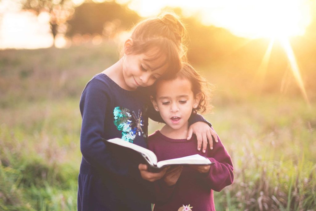 two young girls hugging in a field while reading a book