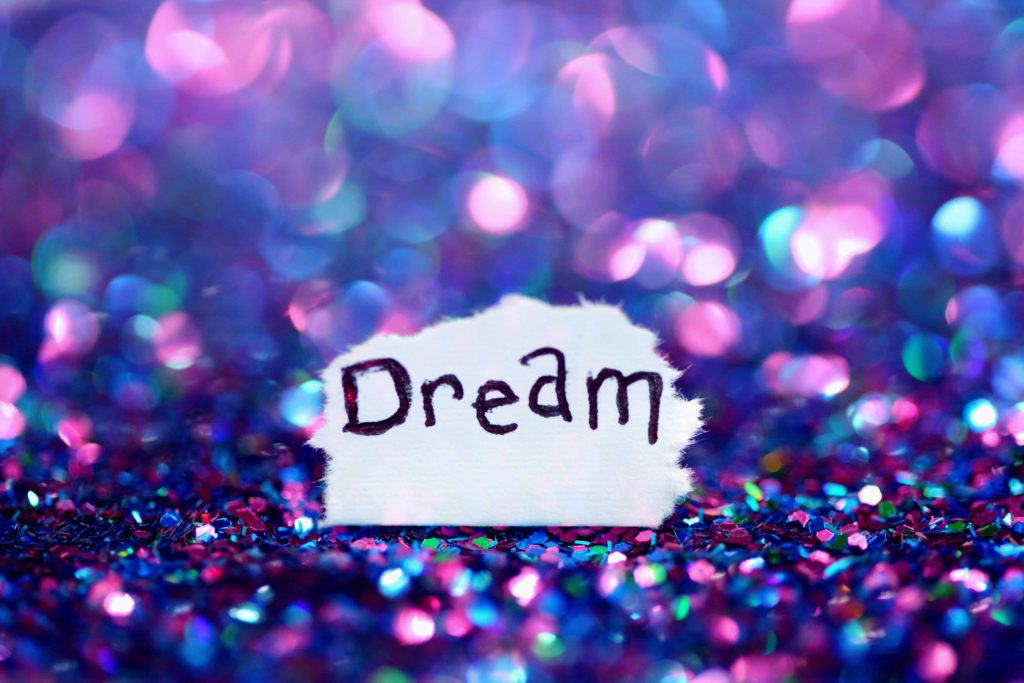 white scrap of paper that says dream surrounded by purple and pink glitter
