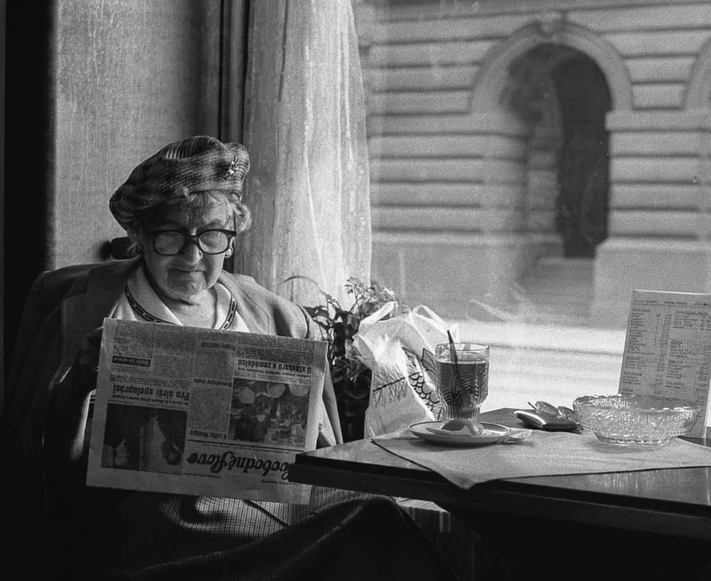 black and white photo of an old woman sitting at table reading a newspaper