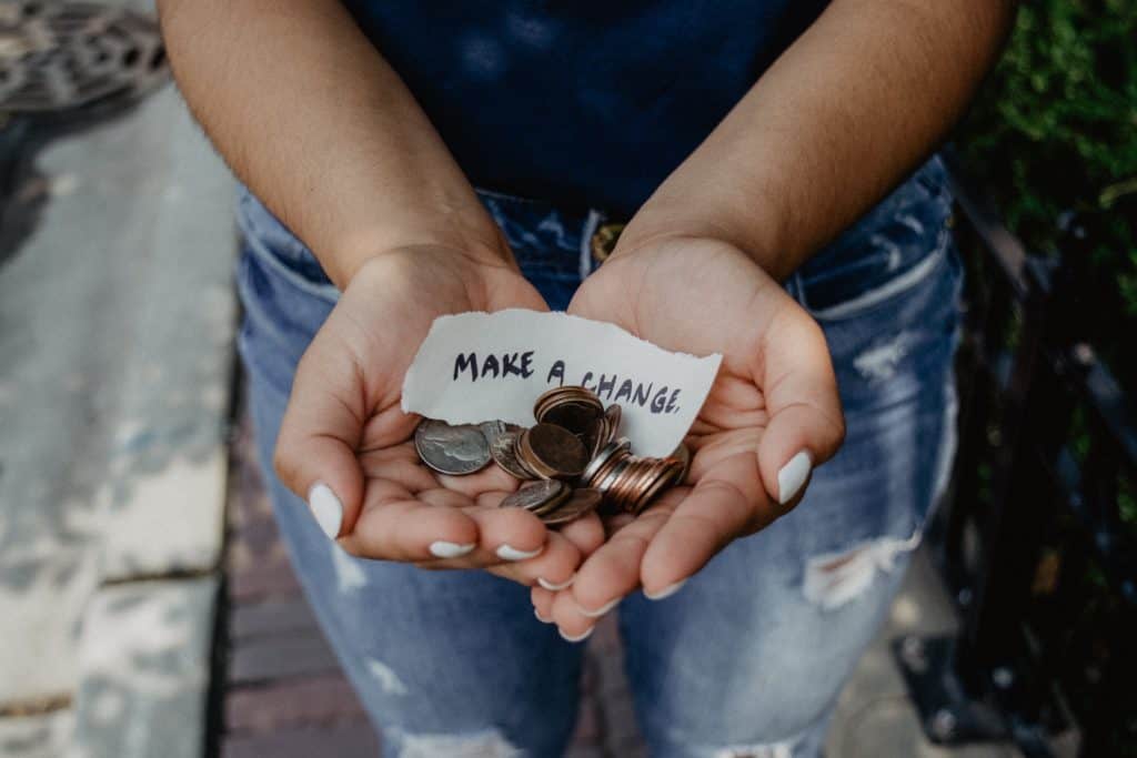Woman holding handful of coins with a small paper sign reading make a change
