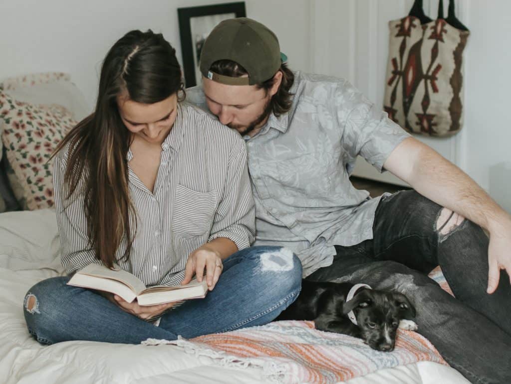 young couple sitting close together on a bed reading a book