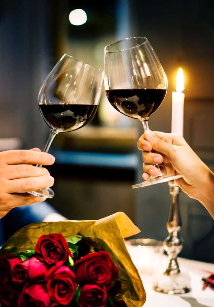 two glasses of red wine touched together over red roses in a cute valentine idea for husband