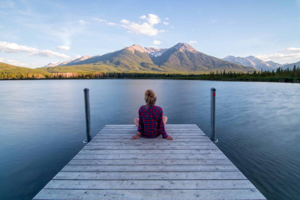 woman sitting on dock overlooking mountain lake to find serenity