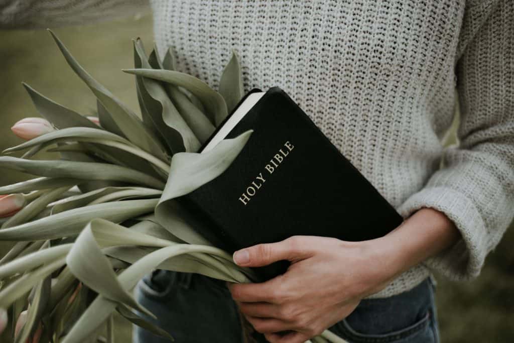woman holding flowers and a Bible to go deeper into gods word to find serenity and find inner peace